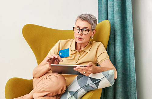 Mature woman in casuals paying by credit card while online shopping from home