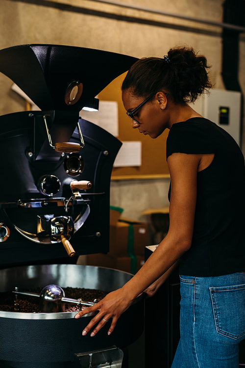 Female business owner standing at modern coffee bean roasting machine