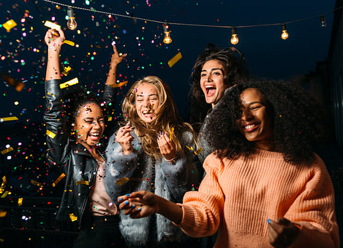 Outdoor shot of group friends laughing under confetti