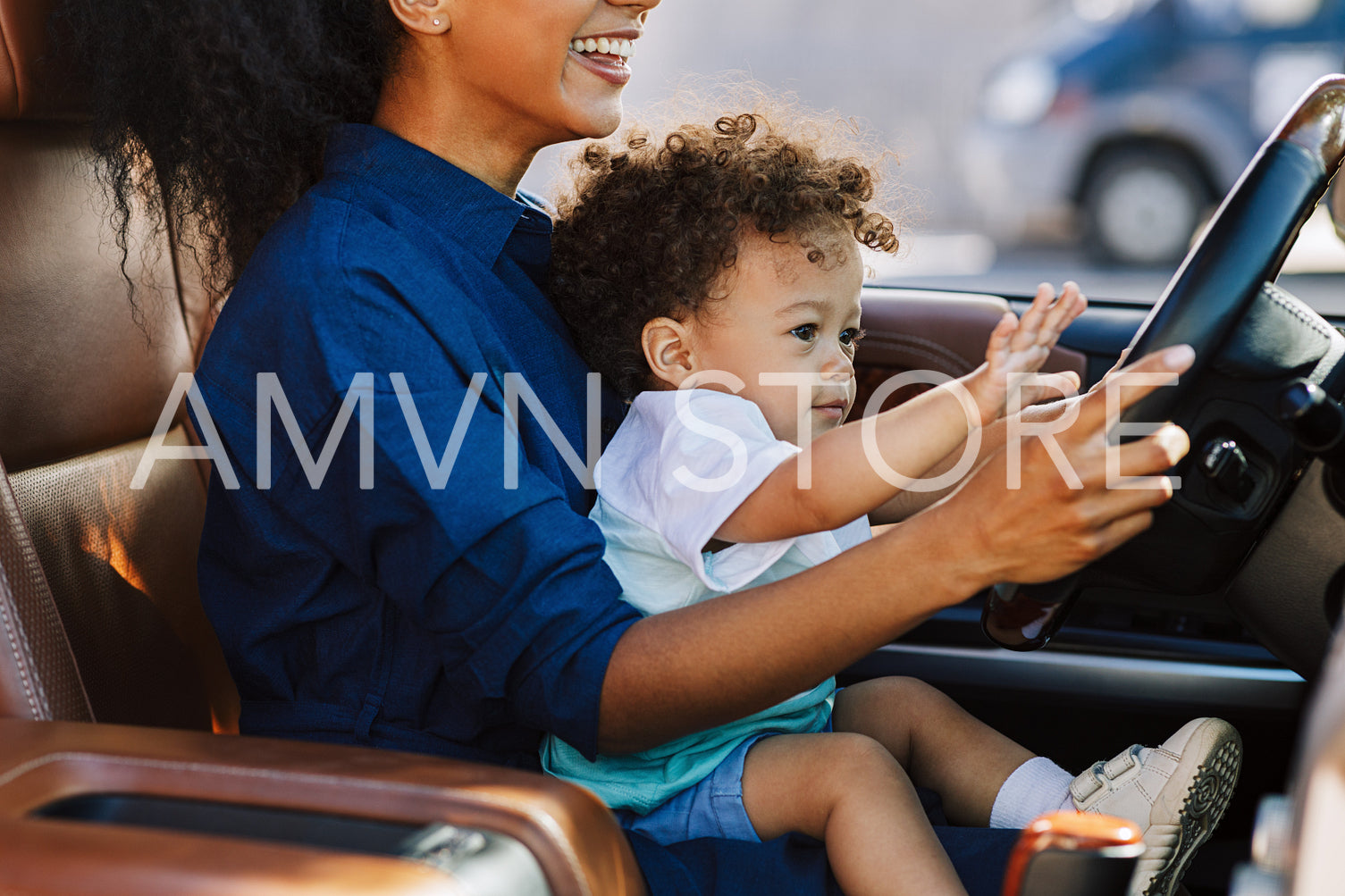 Smiling woman playing with son in a car holding the steering wheel