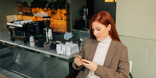 Beautiful female with ginger hair holding a mobile phone. Businesswoman in formal wear typing on a mobile phone.