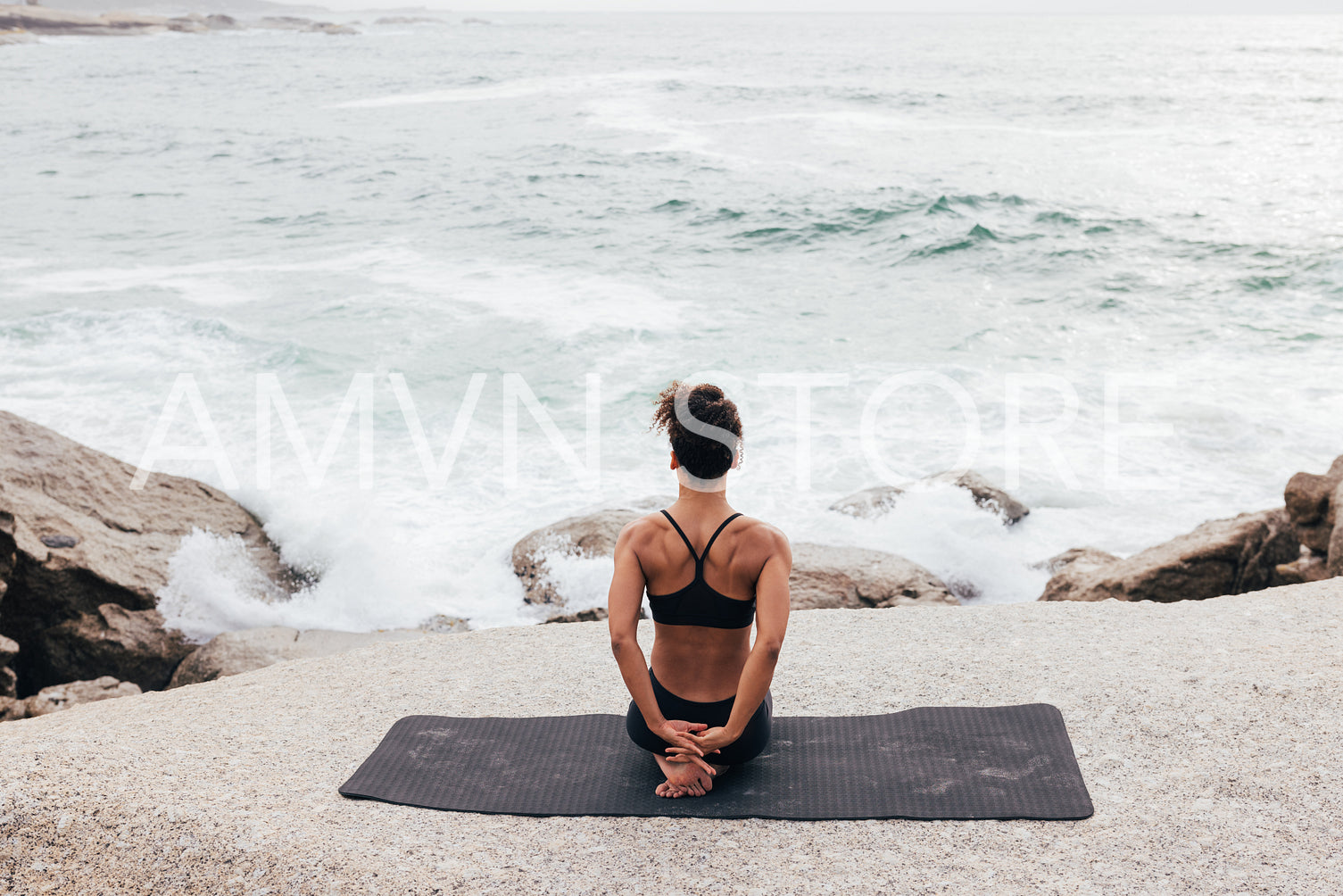 Woman sitting on mat by ocean warming up hands 