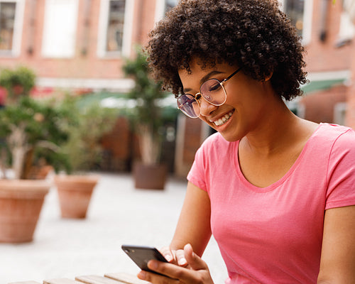 Smiling woman typing on mobile phone while sitting in outdoor cafe