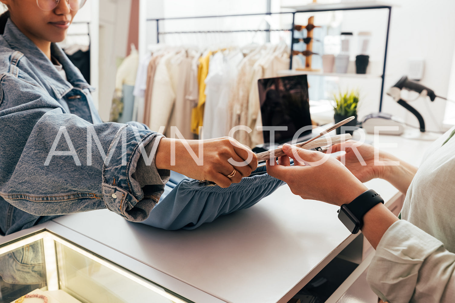 Female buyer giving clothes to unrecognizable clerk for checkout