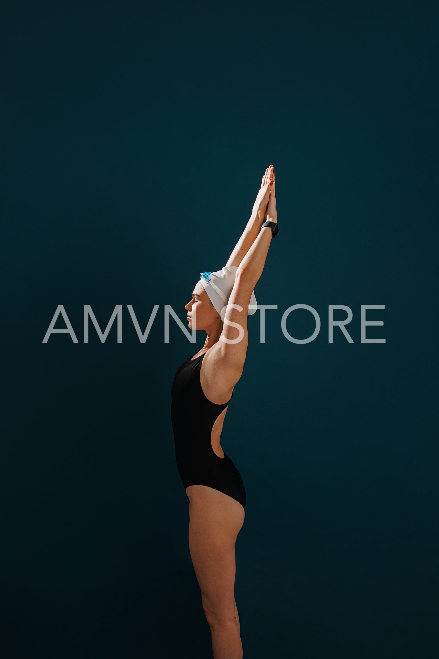 Side view of a young slim female swimmer preparing for competition standing against a blue backdrop