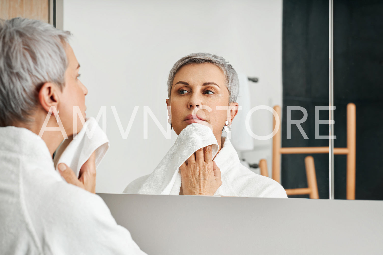 Mature woman standing in front of a mirror wiping her chin with towel	