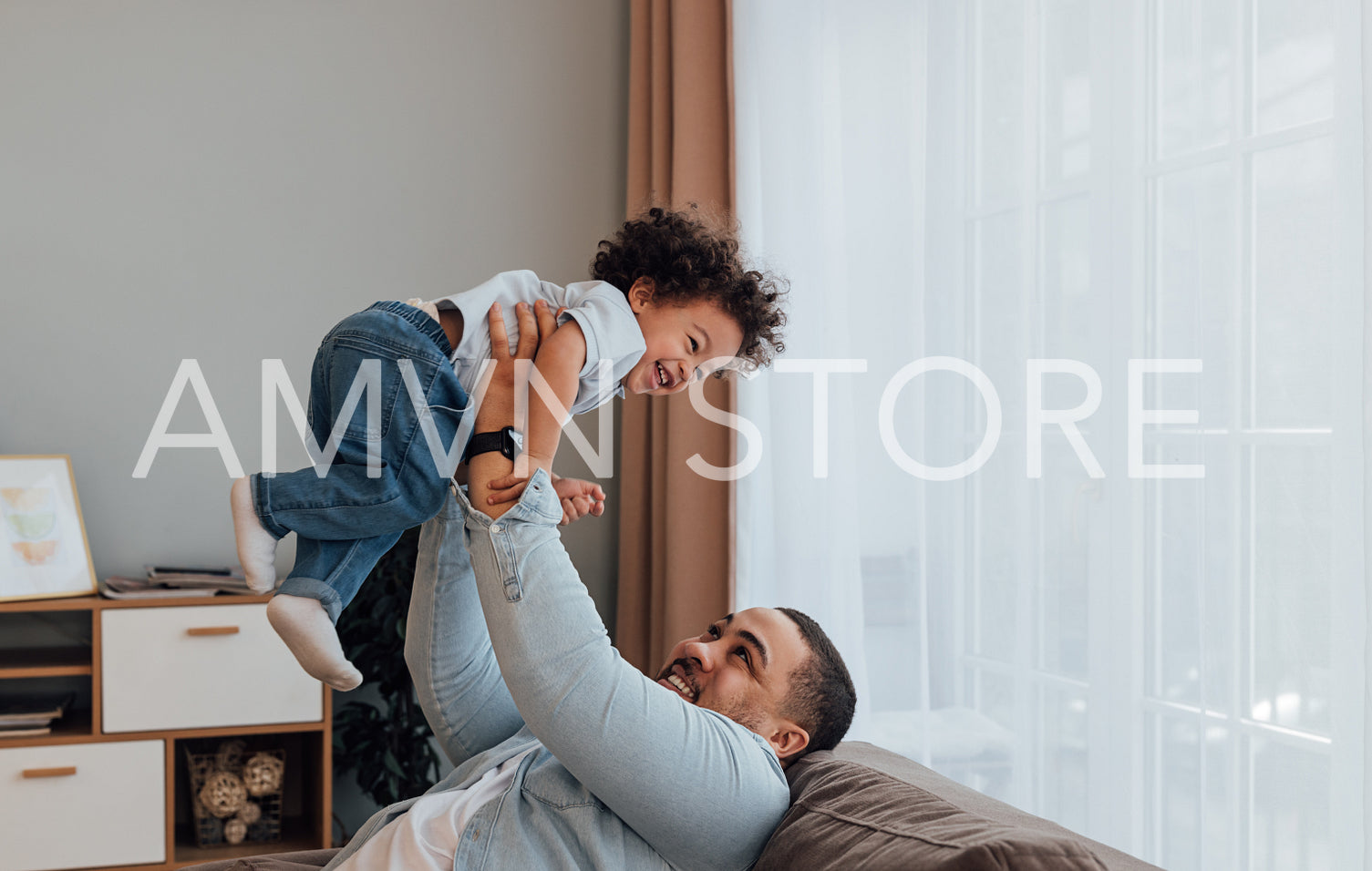 Smiling father lifting his son while sitting on a sofa at home.