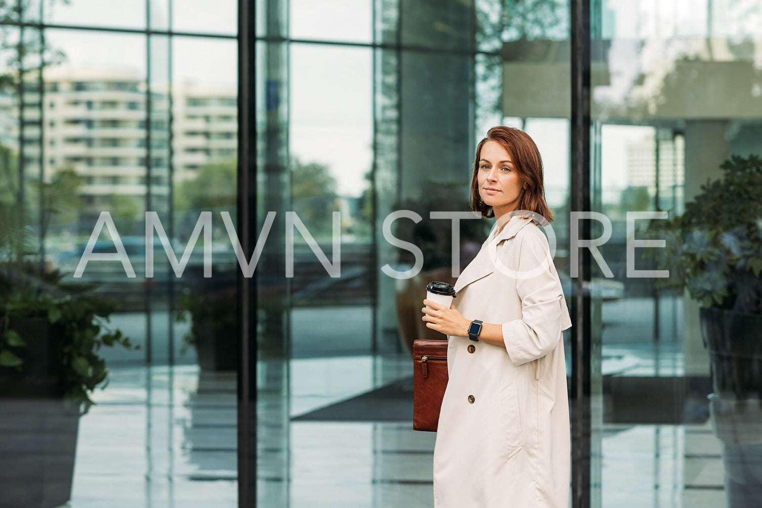 Stylish businesswoman standing at glass building holding a coffee and folder