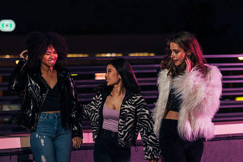 Three cheerful women walking on a roof under neon lights at night