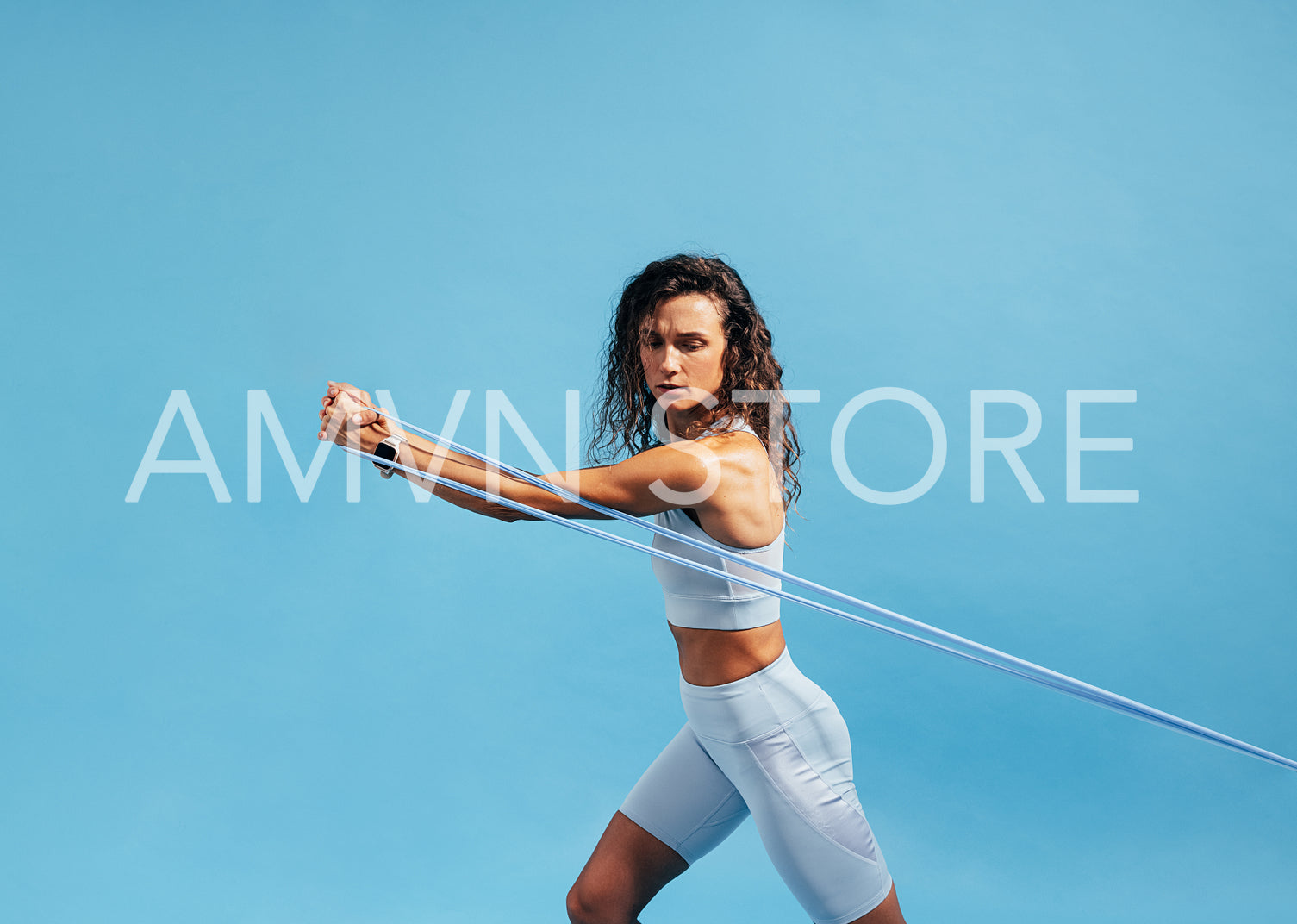 Muscular female in sportswear exercising with resistance band on blue background