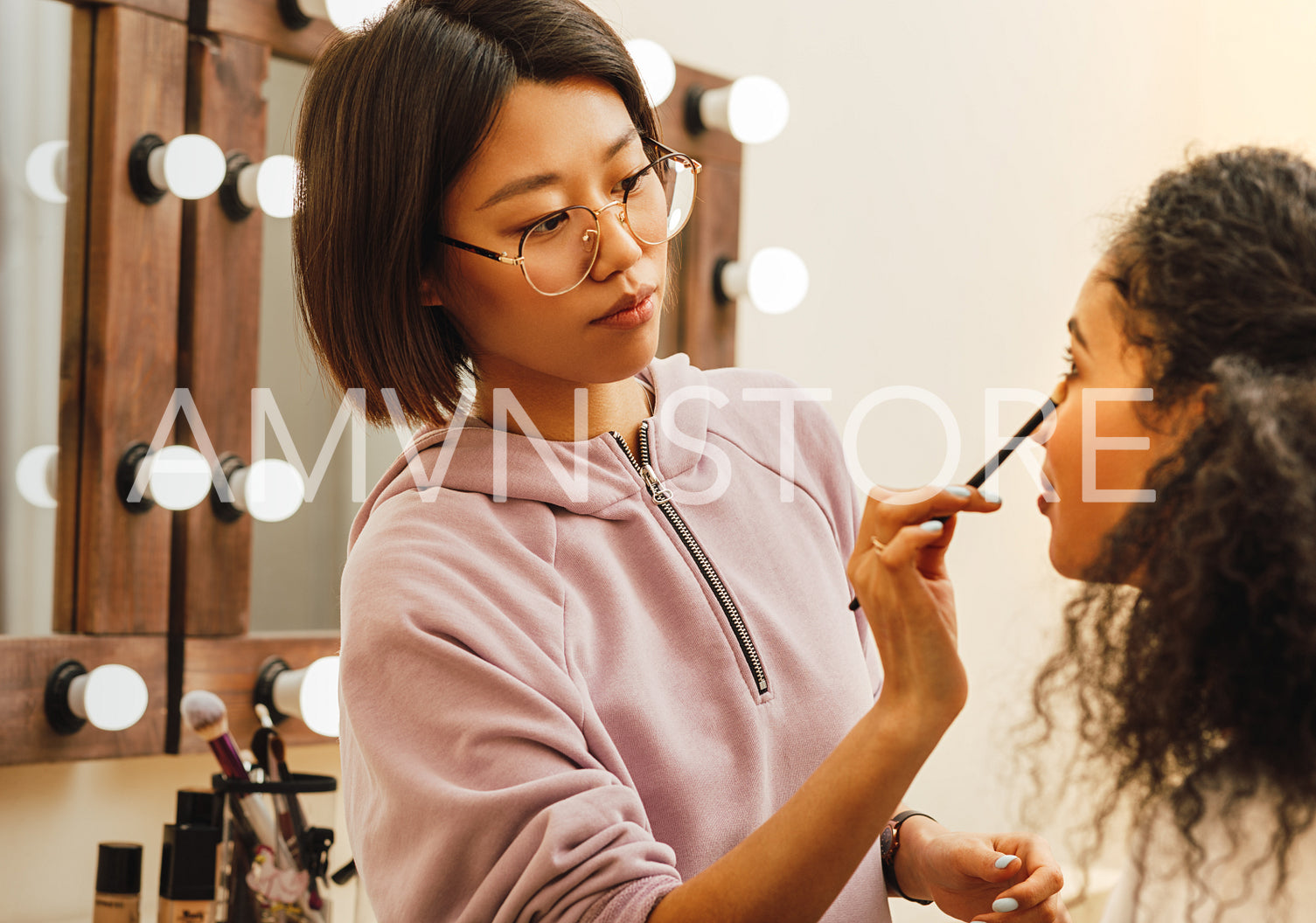 Young woman applying cosmetics with brush on model eye	
