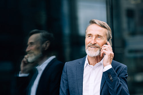 Smiling senior man making call outdoors standing at an office building