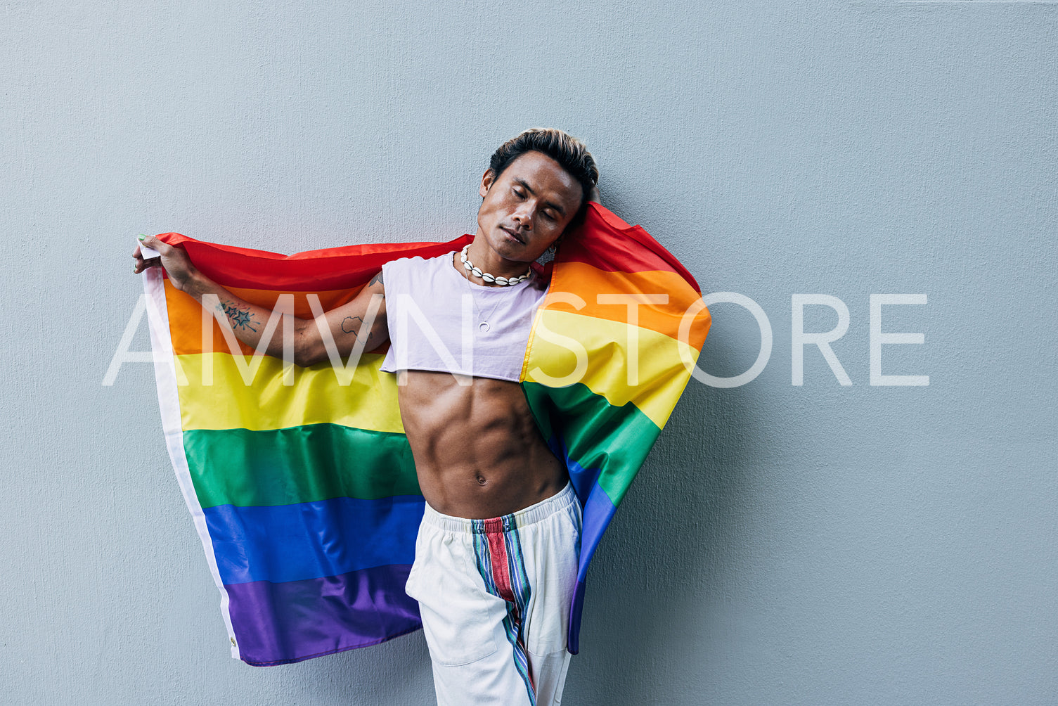 Stylish man with closed eyes leaning a grey wall holding LGBT flag