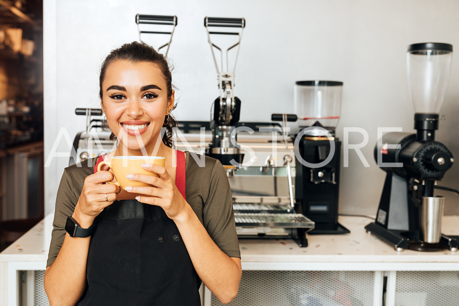 Beautiful cheerful barista holding a mug and looking at camera. Smiling waitress taking a break during a working day.