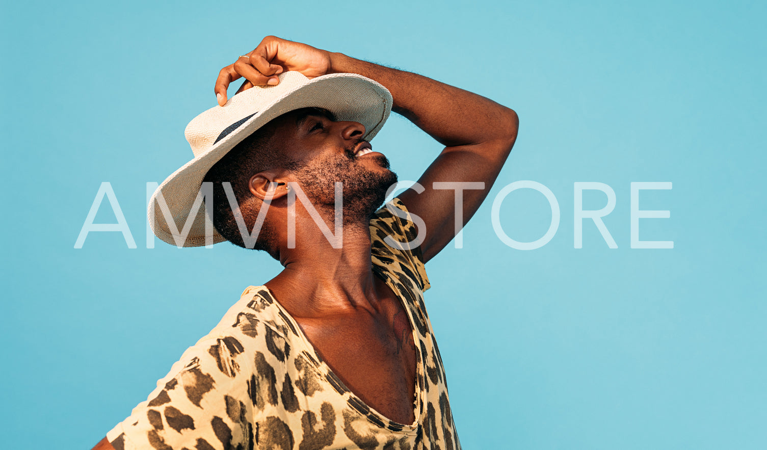 Happy stylish man hiding his face with white straw hat against blue background