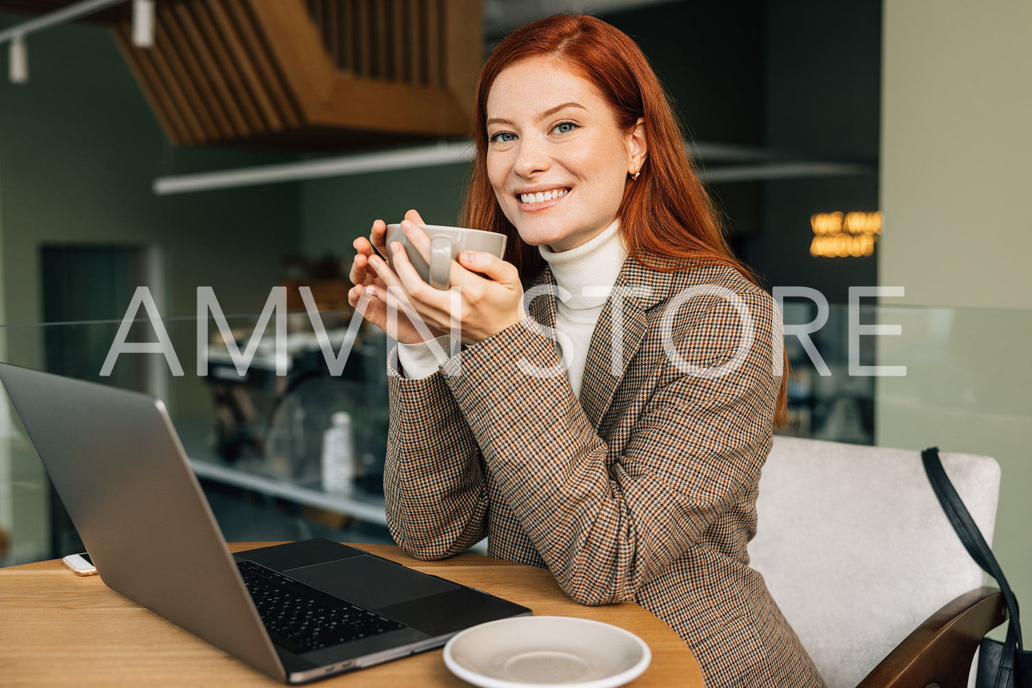 Smiling businesswoman holding a cup of coffee and looking at the camera. Female in business casual clothes sitting at a table in a cafe.