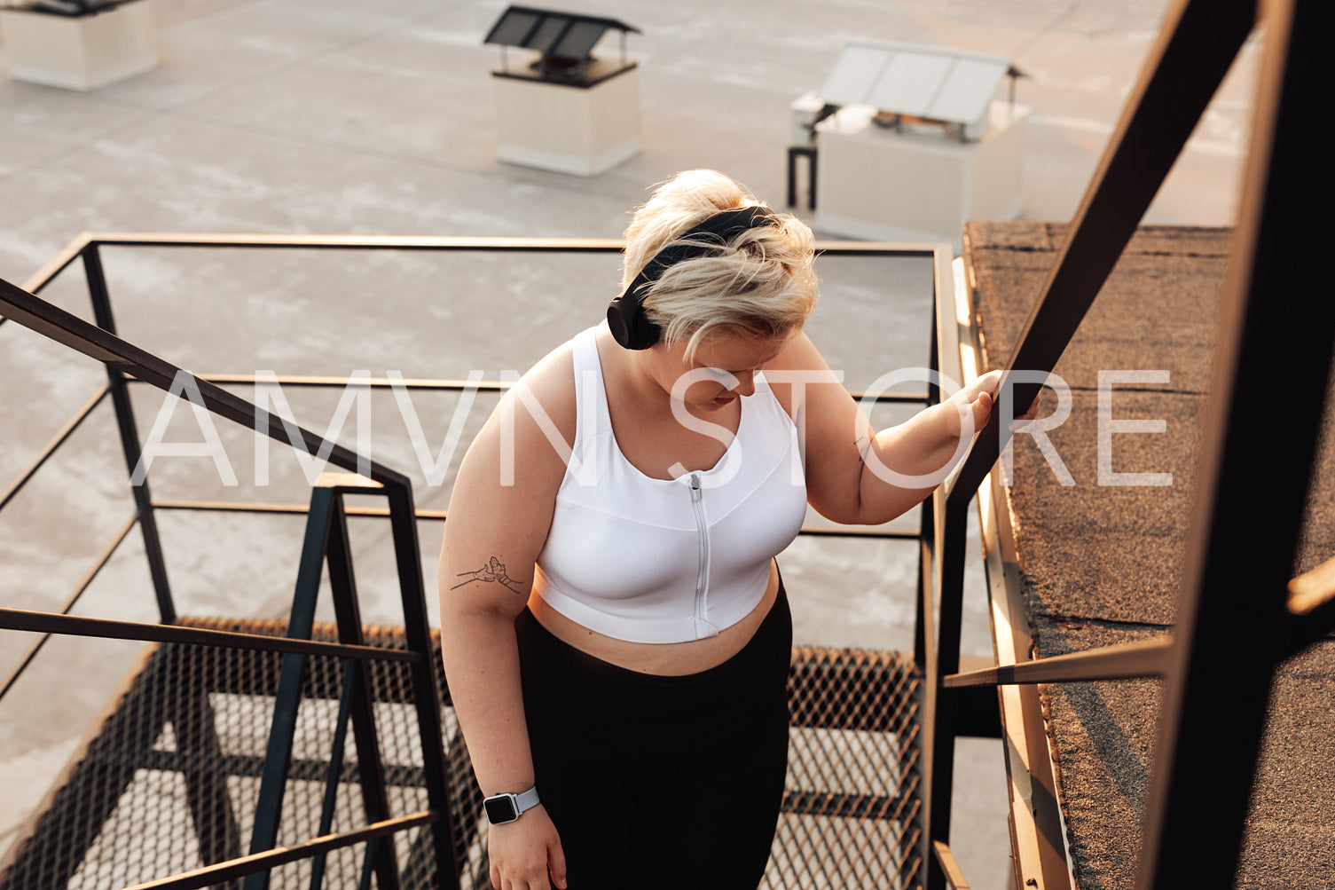 Plus size woman in sports clothes taking a break and looking down while standing on a staircase	