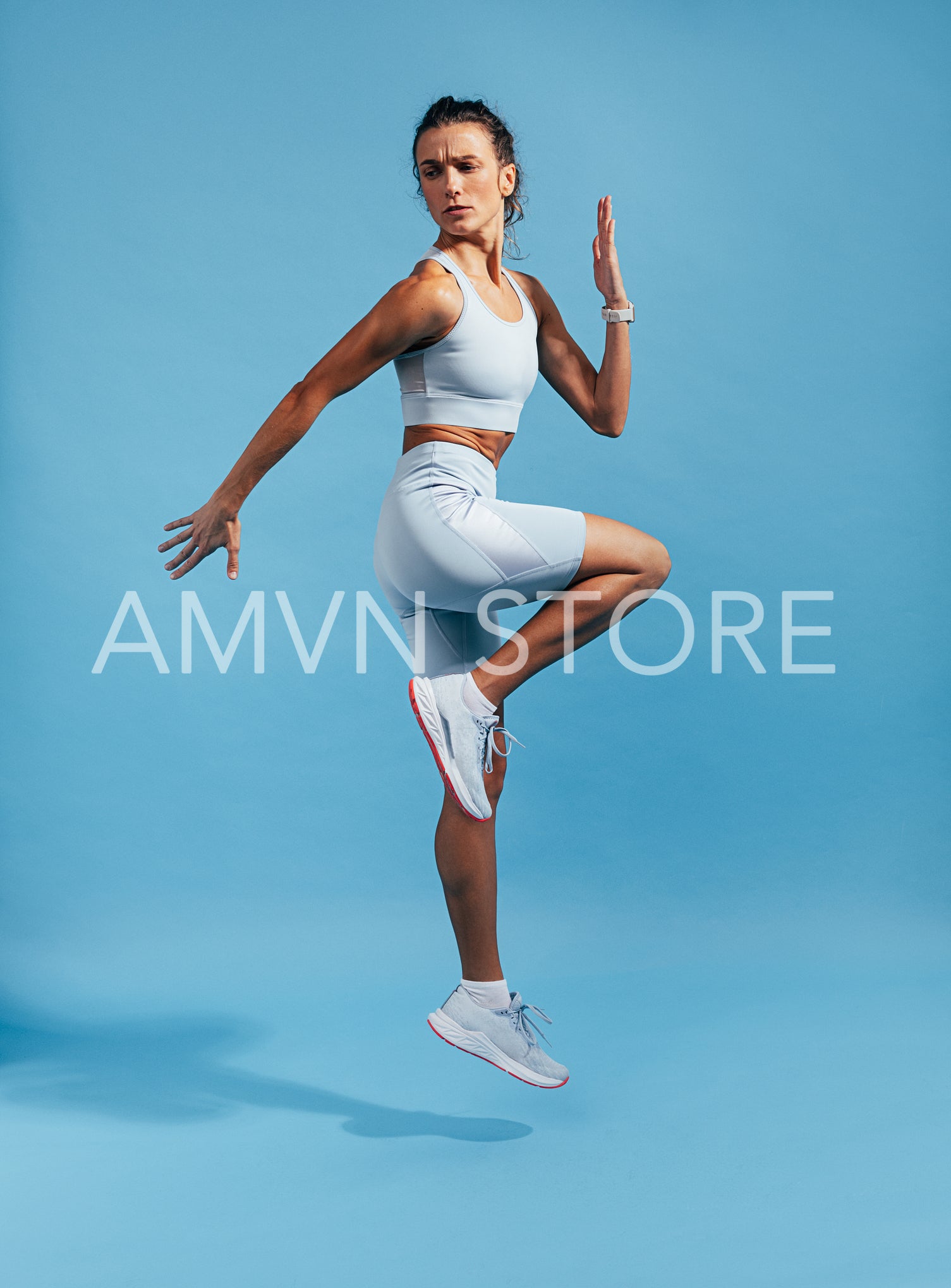 Woman in blue sports clothes jumping. Female sprinter exercising on a blue background.