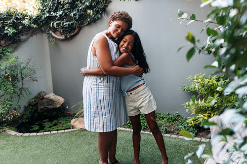 Granny and granddaughter embracing each other while standing in backyard