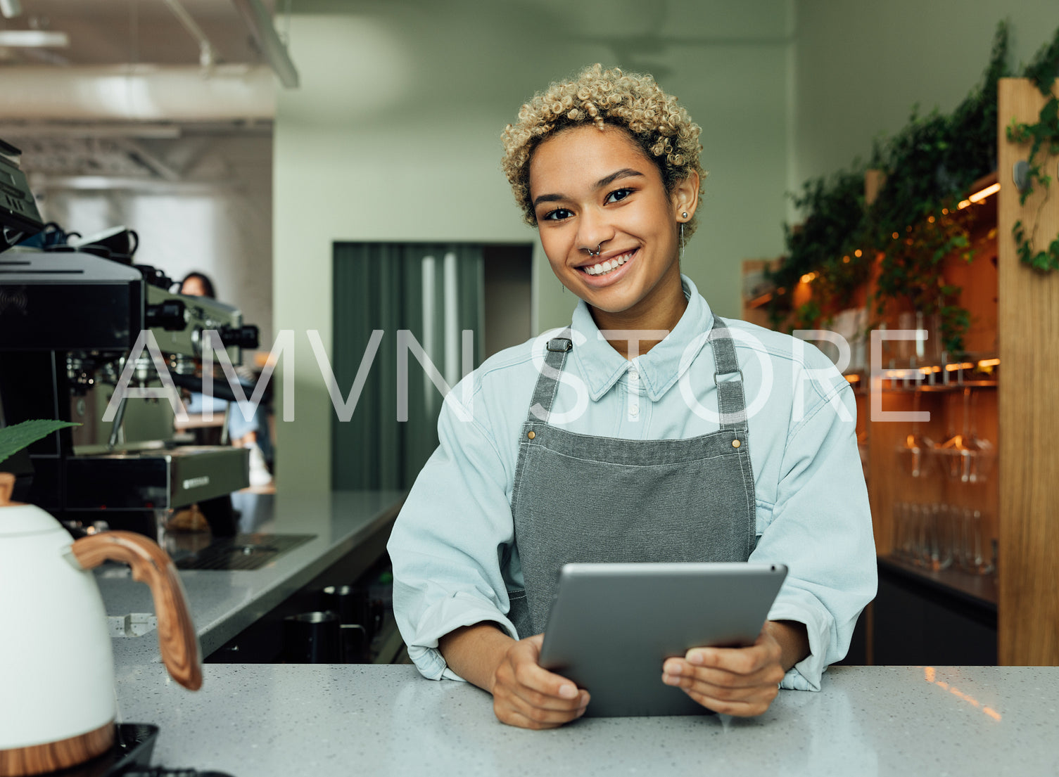 Smiling female barista with digital tablet in the cafe. Portrait of a young female in an apron at a counter in a coffee shop.