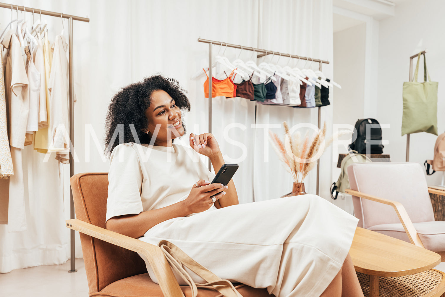 Side view of a stylish customer holding mobile phone while relaxing on armchair during shopping in a boutique