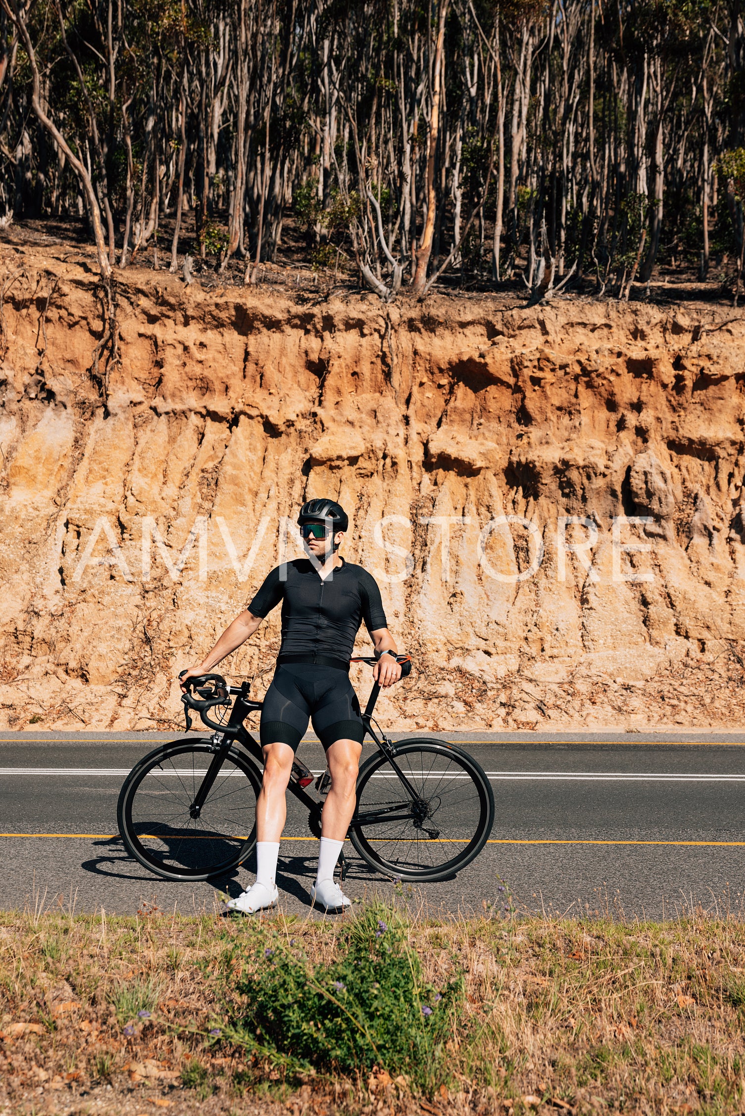 Male cyclist leaning his road bike while standing on a roadside