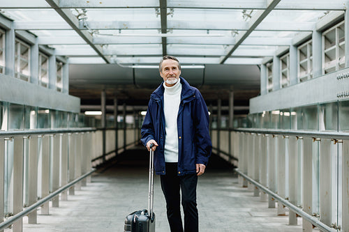 Mature male walking with suitcase on urban background