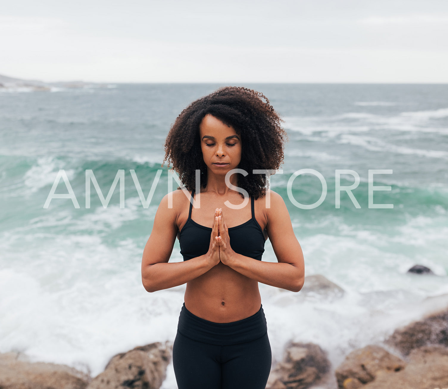 Young female meditating with folded hands while standing by ocean at bay