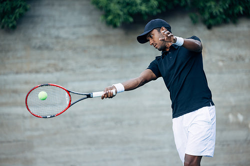 Young tennis player hitting a ball with racket while playing on an outdoor court