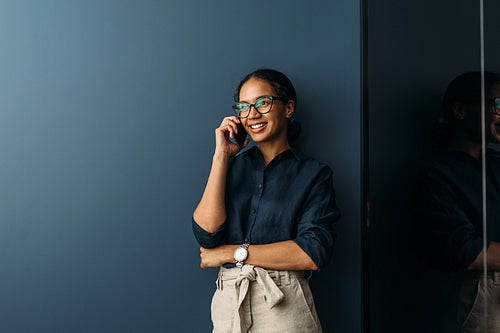 Beautiful smiling businesswoman standing at wall in the living room and talking on cell phone