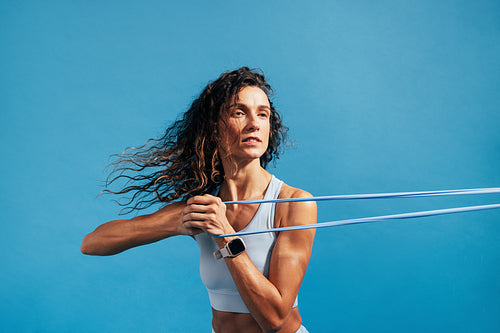 Close up of caucasian woman exercising with a resistance band. Young fitness female training on blue background.