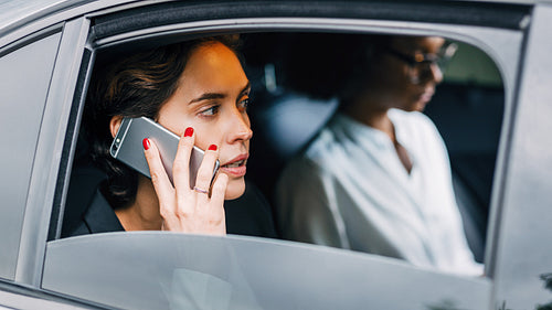 Young woman making a phone call while sitting on a backseat of a taxi