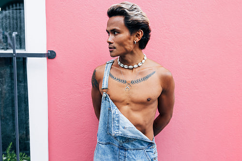 Young stylish man standing outdoors near a house with pink wall and looking away