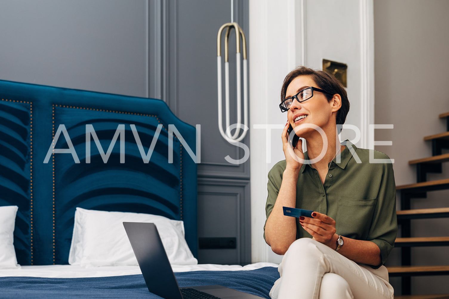 Mid adult woman talking on mobile phone and holding a credit card. Businesswoman making online order while sitting in a luxury apartment.	