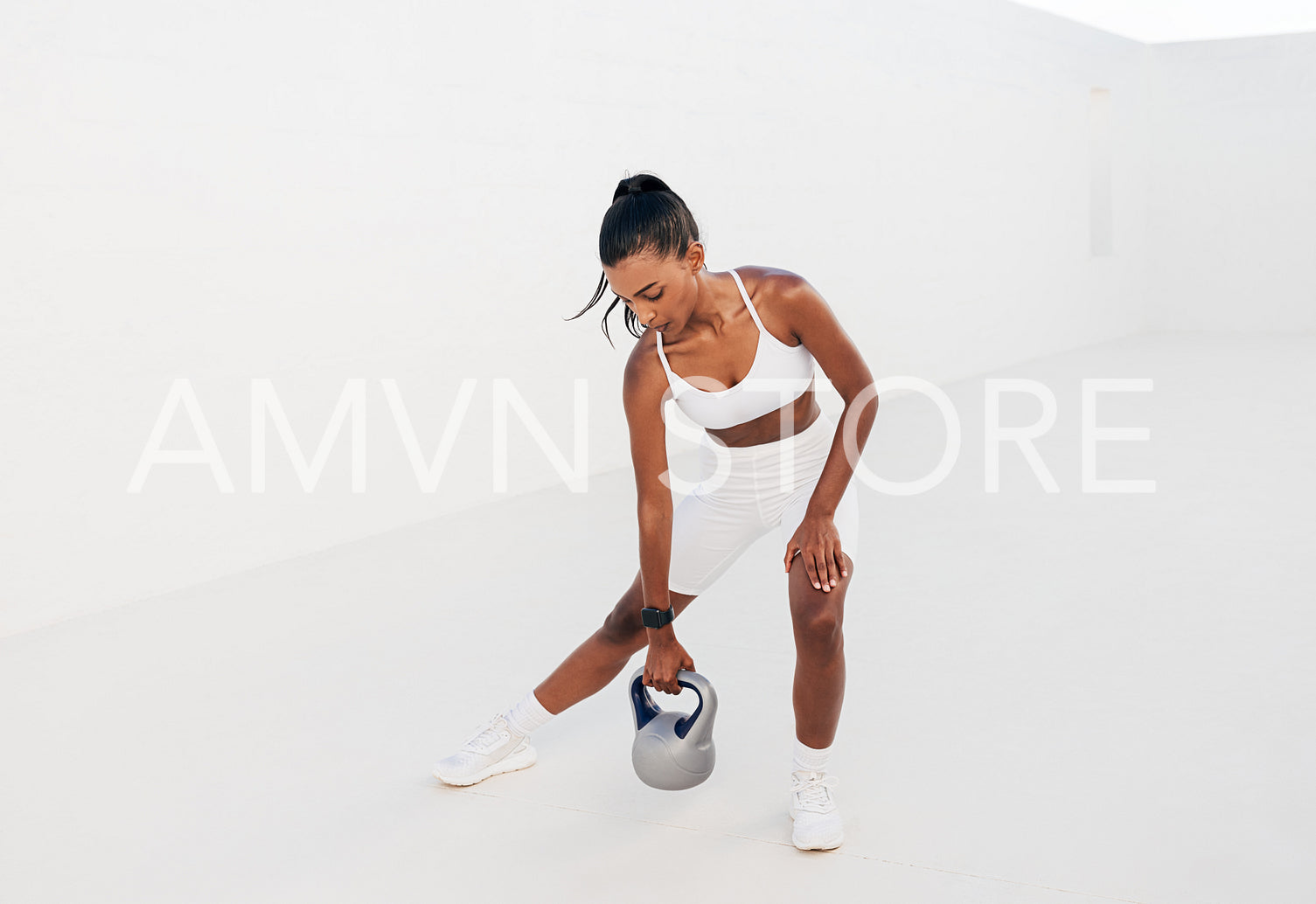 Slim female in a white sports bra doing intense training with a kettlebell. Full length of a fitness influencer outdoors.