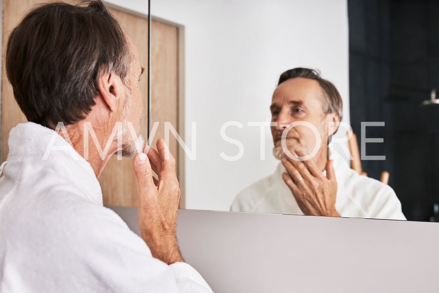 Senior man touching his chin in bathroom in front of a mirror	