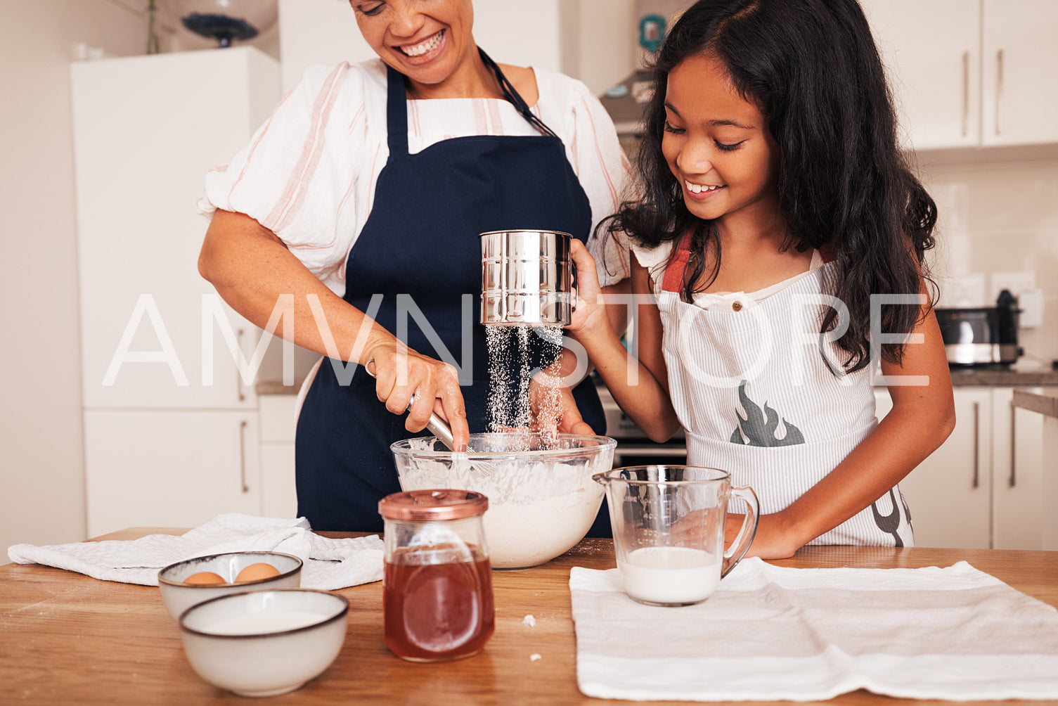 Senior woman and granddaughter sifting flour at a table in kitchen. Girl and her grandma making dough.