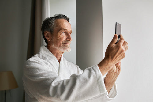 Senior man taking photographs on his smartphone from a hotel room