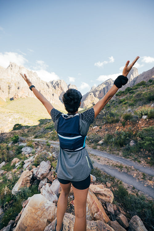 Rear view of young female standing in valley with raised arms. Young woman enjoying hike.