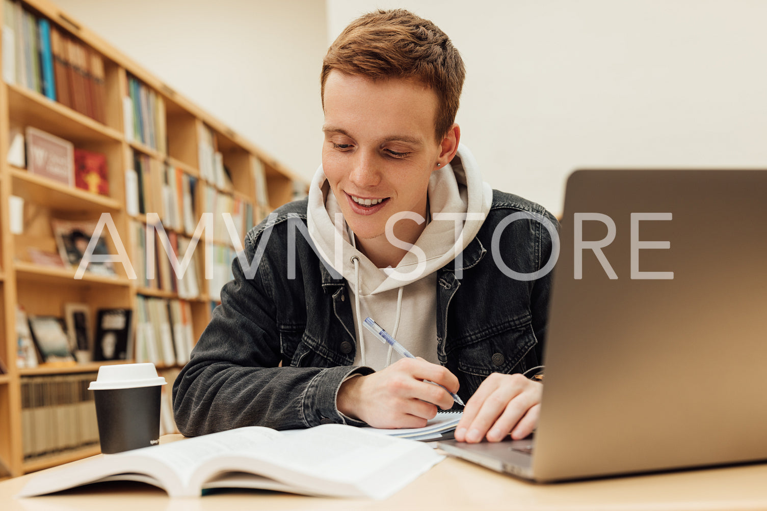 Smiling male student looking at notes while sitting at desk and preparing exams