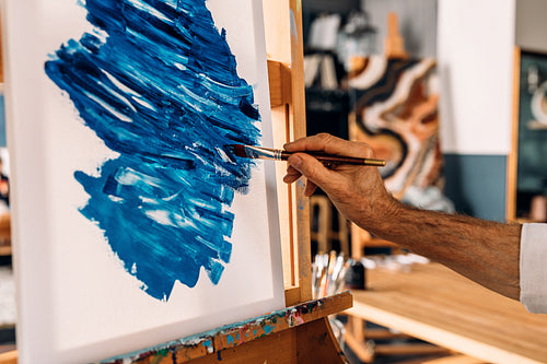 Hand of a painter holding a brush and drawing on canvas