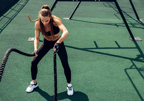 Young muscular woman exercising with battle ropes on rooftop. Female working out outdoors with ropes.