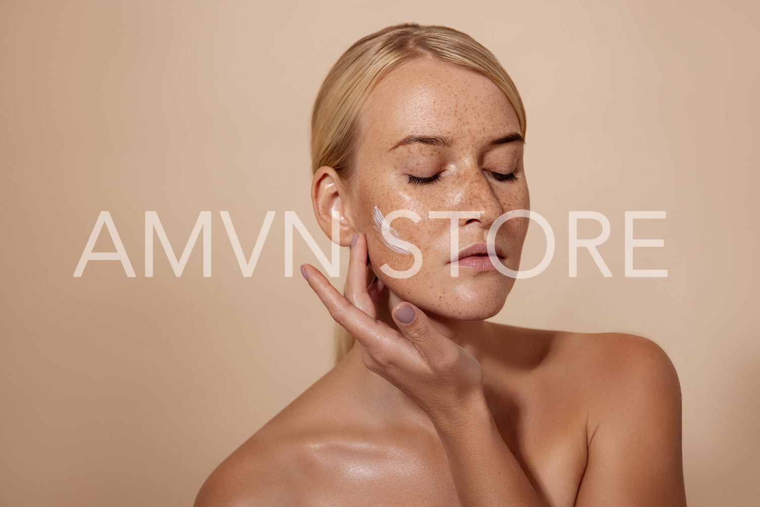 Caucasian woman applying facial moisturizer standing in studio against pastel background