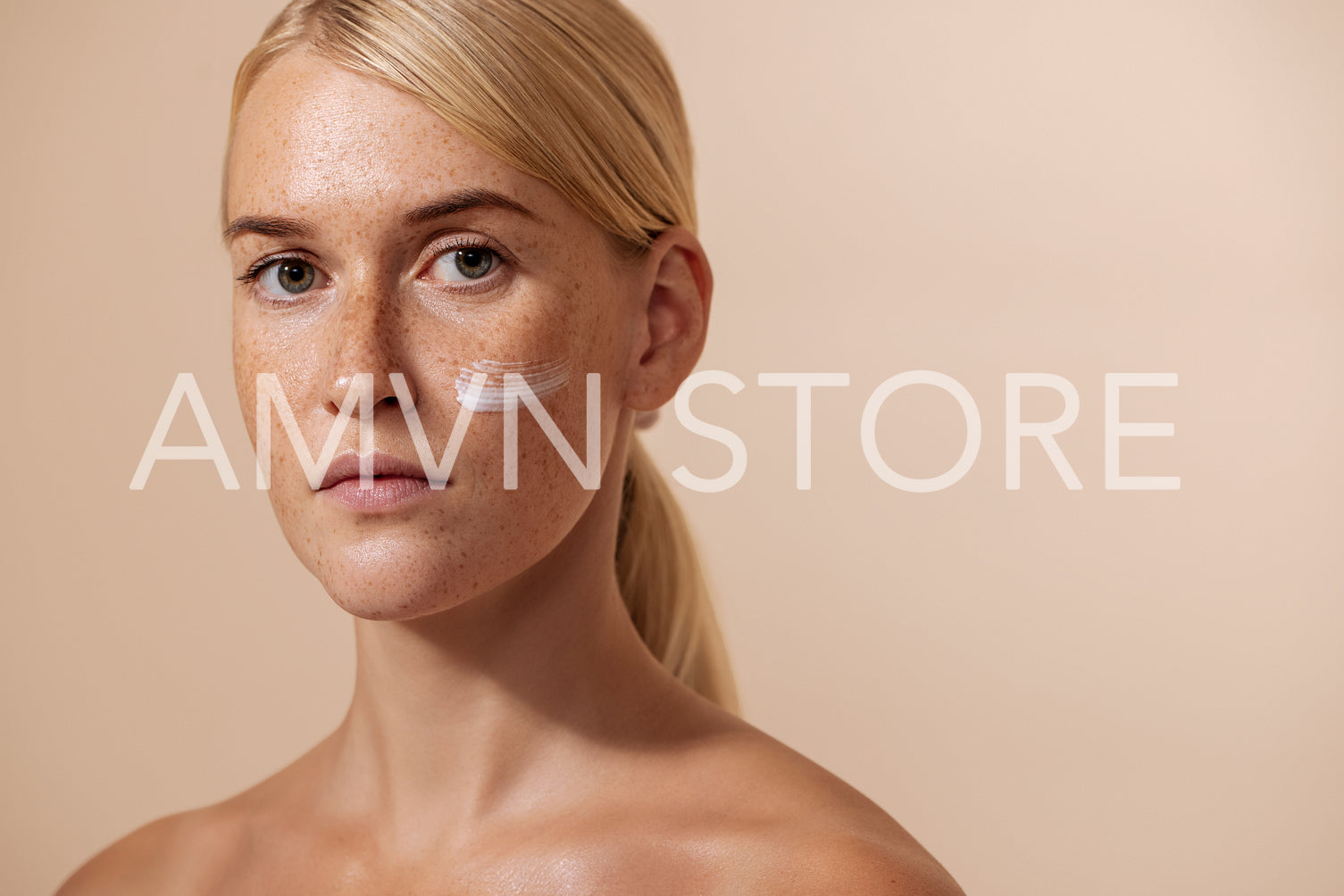 Beautiful blond woman with moisturizer on her face looking straight of a camera in studio