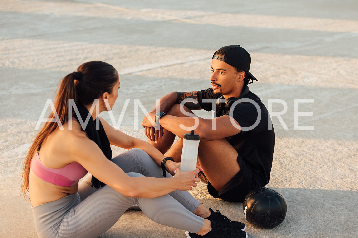 Fitness couple taking a break during workout sitting together on the roof at sunset