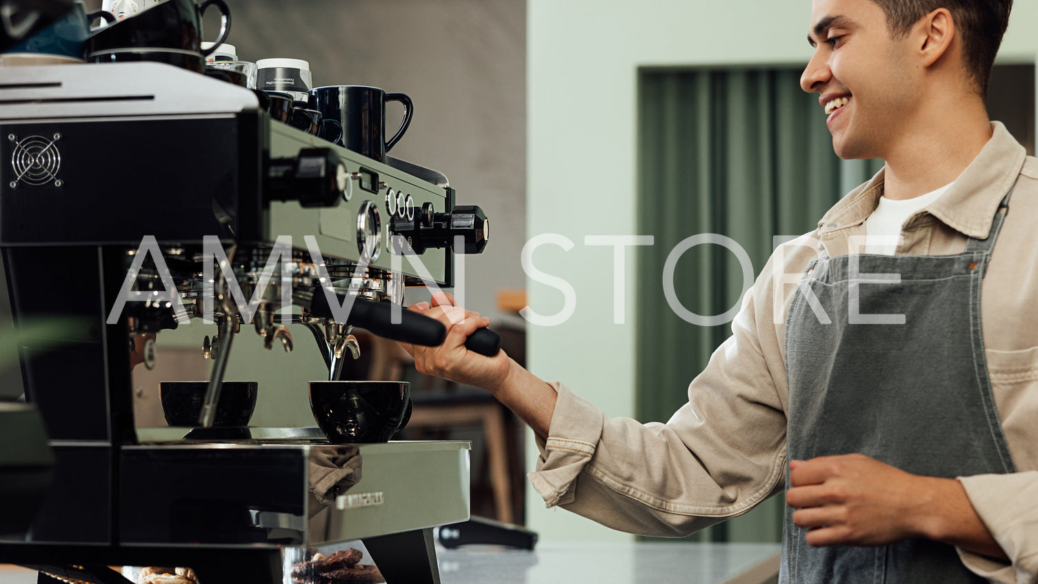 Cropped shot of a young barista using a coffee machine. Smiling male barista adjusting coffee machine.