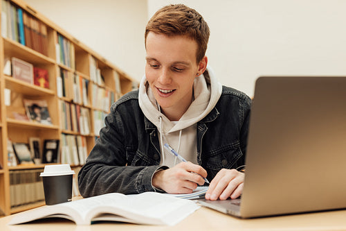 Smiling male student looking at notes while sitting at desk and preparing exams