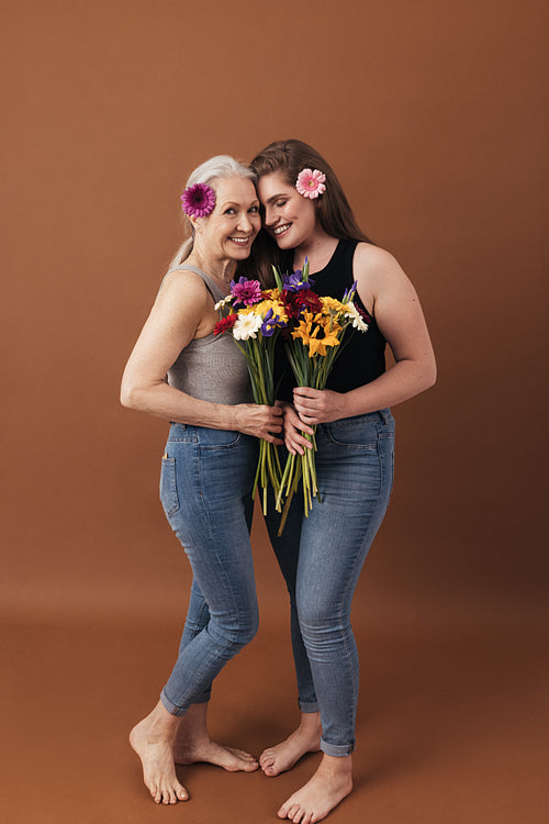 Two women with flowers posing in a studio a brown background