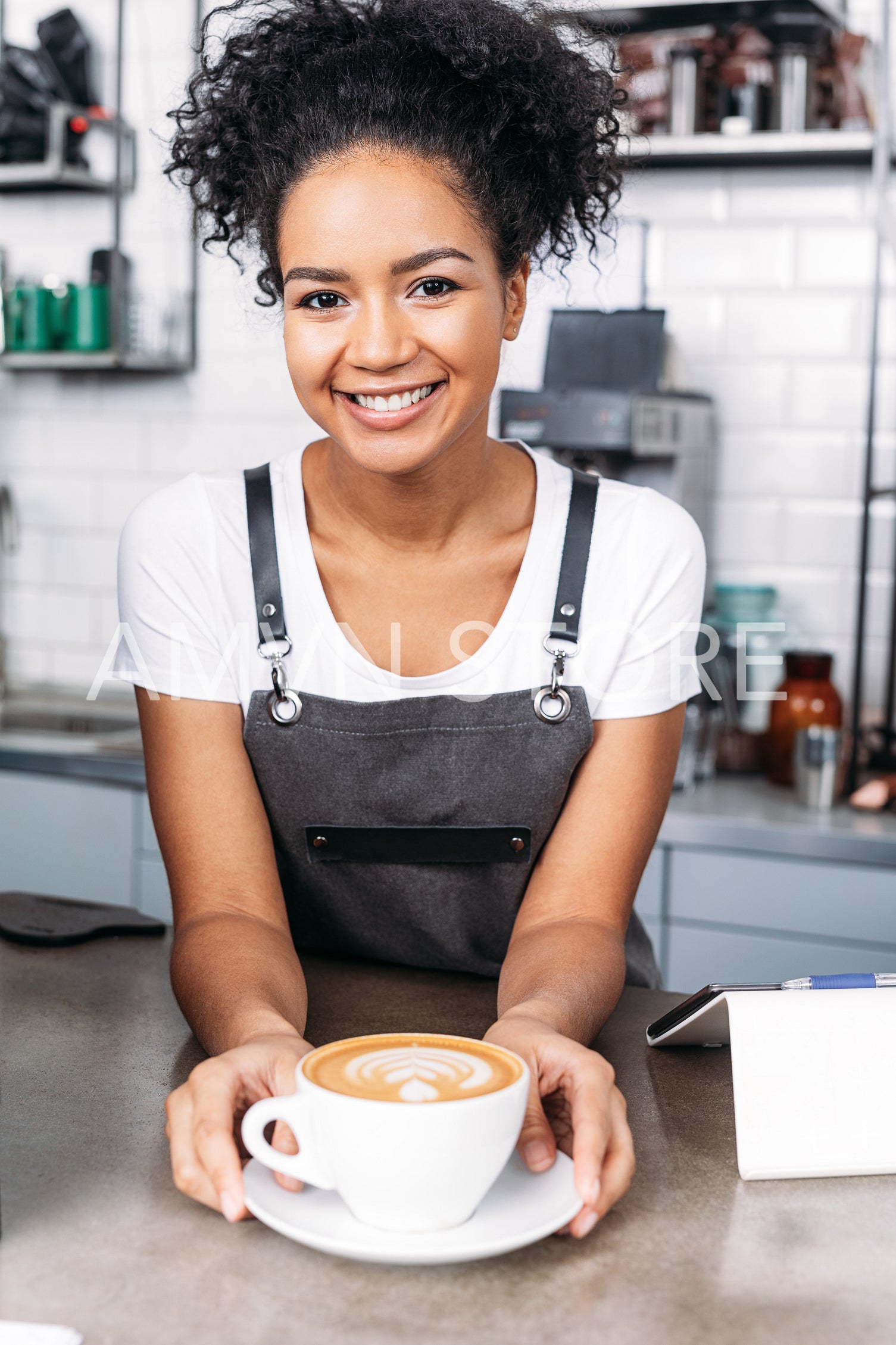 Smiling waitress with curly hair with a freshly prepared cappuccino at the counter 