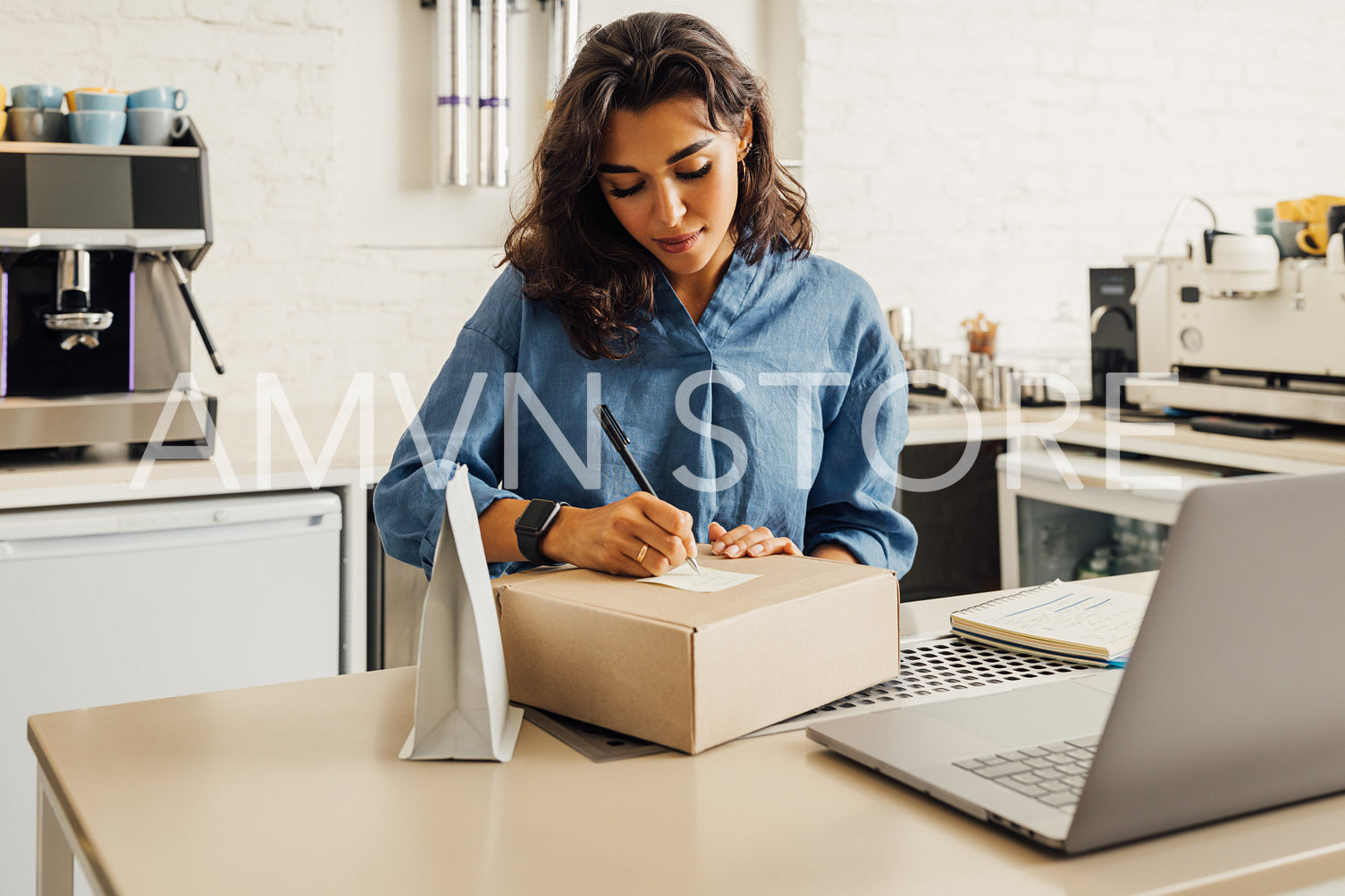 Young businesswoman standing in her cafe preparing parcel with coffee for shipping. Entrepreneur writing on a sticker on a cardboard box.